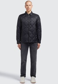 Sort quiltet jakke med knaplukning, der har krave og mønsteret polstring. Kombineret med grå jeans og hvide sneakers.