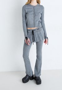 Szary dzianinowy krótki kardigan z guzikami, w połączeniu z plisowaną szaro-skalną spódnicą z troczkami. Czarne platformowe klompy dopełniają zestaw.