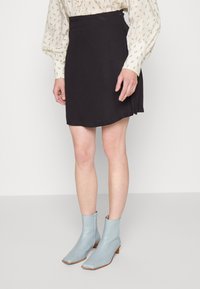 Saia A-line preta em tecido suave e com um caimento sutil, combinada com botas de tornozelo azul claro com bico quadrado e salto baixo.