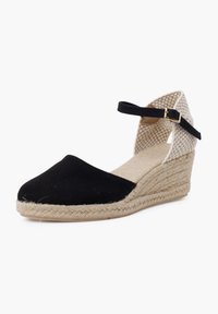 Black canvas wedge shoe with a jute rope sole, featuring a woven beige ankle strap and a slight pointed toe design. Accented with a gold buckle.