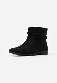 Botas de tobillo negras hechas de suave ante con un diseño arrugado, punta redonda y tacón bajo. Textura suave y detalles de costura mínimos.