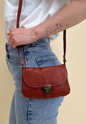 Bruine leren schoudertas met een klep en een metalen sluiting. Kenmerkt zich door een gladde textuur en een slank formaat. Draagt op een met denim beklede taille.