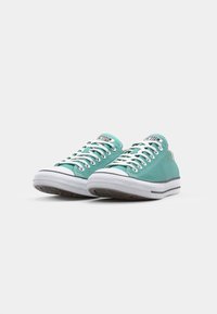 Turquoise canvas sneakers with white laces, rubber outsole, black accents along the sole, and logo label on the tongue. Classic low-top design.