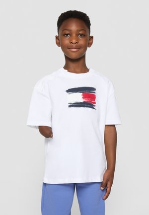 Tricou alb din bumbac cu mâneci scurte, prezentând un design cu pensule multicolore în albastru închis, roșu și alb pe piept.