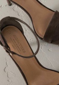 Smešane smeđe zamršene sandale s visokom petom i tankim remenom oko gležnja, bež uložak s utisnutim natpisom "SIGNATURE MADE IN BRAZIL", minimalistički dizajn.