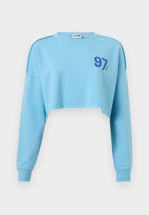 Lyseblå cropped sweatshirt med lange ærmer og blå "97" trykt på venstre bryst.