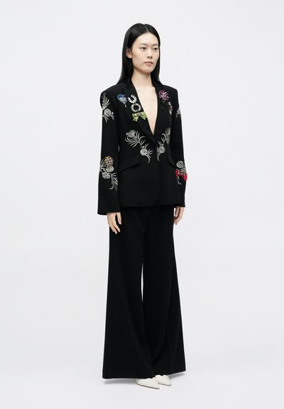 Fekete blézer, virágmintás hímzéssel, több színben, széles szárú fekete nadrággal párosítva. A szettet fehér, hegyes orrú cipő egészíti ki.