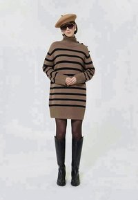 Robe-pull à rayures marron et noires avec col montant, poignets et ourlet côtelés. Associée à des bottes noires montantes jusqu'au genou et un béret beige.