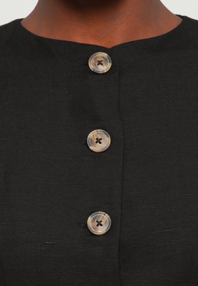 Black fabric garment with a round neckline, featuring three round buttons with four holes, displaying a smooth, slightly textured surface.