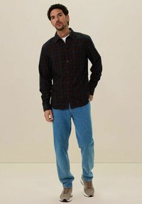 Heren overhemd met knopen in een zwart blauwe, rode en zwarte ruit, gecombineerd met lichtblauwe spijkerbroek en grijze sneakers. Glad stof, relaxte pasvorm.