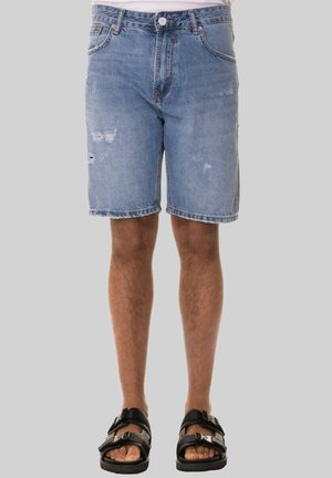 Shorts in denim chiaro con dettagli strappati, taglio dritto, design a cinque tasche e orlo sfilacciato, abbinati a sandali neri.