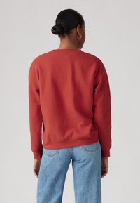 Sweat-shirt rouge avec un col rond et des manches longues, fabriqué en tissu doux. Présente des poignets et un ourlet côtelés, associé à un jean bleu.