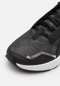 Svart och vit sko med tådel i texturerat mesh, svarta snören och en liten silverreflekterande detalj nära sulan.