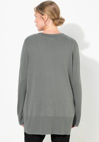 Lång, oversized tröja i mjukt, mörkgrönt stickad tyg. Har ribbad halsringning och mudd, med klyvd fåll och avslappnad passform.