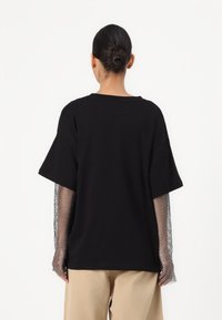 Melna īsām piedurknēm krekls ar brīvu piegriezumu, kam ir caurspīdīga sērfota piedurkne un apaļa kakla izgriezums. Gluda auduma ar nemanāmu logo detaļu aizmugurē.