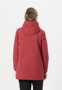 Jachetă impermeabilă roșie cu glugă, mâneci lungi și manșete elastice. Textură netedă și tăietură lejeră, ajungând până la mijlocul coapsei.