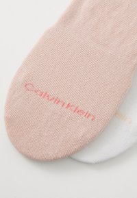 Divi pāri potīšu zeķu; viens rozā ar 'Calvin Klein' sarkanā krāsā un viens balts ar 'Calvin Klein' dzeltenā krāsā. Gluda tekstūra, elastīgs pielāgojums.