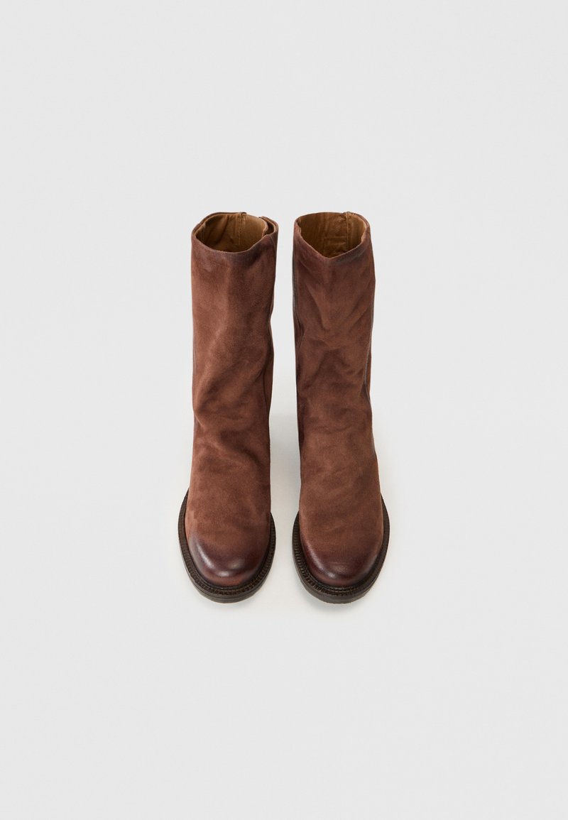 Une paire de bottes en daim marron mi-mollet avec des pointes arrondies et des semelles noires, présentées debout sur un fond clair uni.