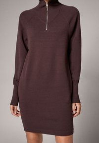 Bordowa dzianinowa sukienka z wysokim kołnierzem, srebrnym zamkiem błyskawicznym i długimi rękawami. Posiada dopasowany krój z prążkowanymi mankietami i dołem.