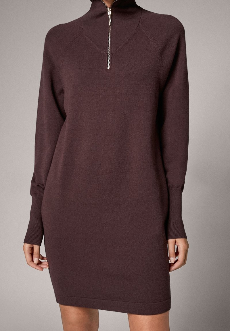 Bordowa dzianinowa sukienka z wysokim kołnierzem, srebrnym zamkiem błyskawicznym i długimi rękawami. Posiada dopasowany krój z prążkowanymi mankietami i dołem.