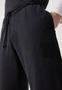 Black cotton joggers with an elastic waistband, featuring a small embroidered "HUGO" logo on the left leg. Smooth texture, relaxed fit.