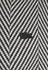 Svart och vit chevronstickad mönster med en liten svart broderad krokodil-logotyp i mitten.