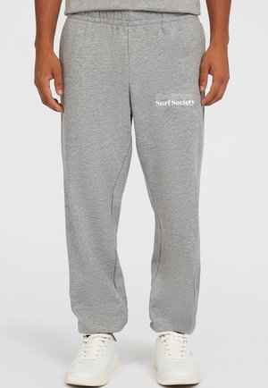 Pantalones de chándal grises con una cinturilla elástica, costuras laterales y texto gráfico blanco "Surf Society" en el muslo izquierdo. Tejido suave y casual.
