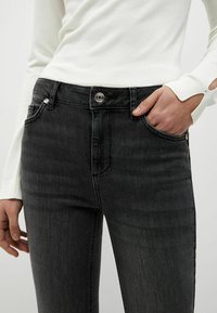 Juodi džinsai, slim fit kirpimo, vidutinio aukščio juosmuo, sidabriniai aksesuarai, penki kišenės ir subtilus išblukimas priekyje ir gale.