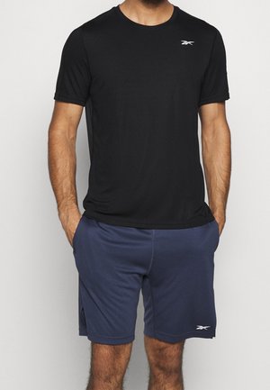 Camiseta atlética negra de manga corta con cuello redondo, combinada con pantalones cortos azul marino que tienen una cinturilla elástica y bolsillos laterales. Logotipo blanco en la camiseta.