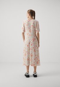 Rochie midi florală dintr-un material ușor, având un fundal pastelat cu modele colorate. Mâneci scurte și o tăietură lejeră. Pantofi cu talpă platformă negri.