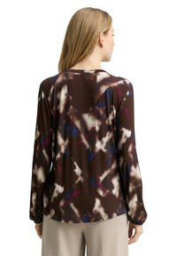 Braunes Langarmshirt mit Muster und abstrakten Designs in Weiß, Blau und Burgunderrot. Mit rundem Ausschnitt und elastischen Bündchen.