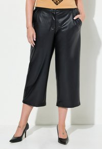 Culottes in finta pelle nera con una vestibilità rilassata, dotati di tasche laterali e una superficie liscia, abbinati a tacchi a punta neri.