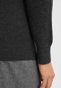 Dunkelgrauer, gerippter Strickpullover mit langen Ärmeln und engem Bund, kombiniert mit einer hellgrauen, filzigen unteren Schicht.