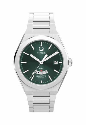 Strieborné kovové hodinky značky Timex s zeleným ciferníkom, bielymi hodinovými značkami, okienkom na dátum a subciferníkom GMT na pozícii 6 hodín.