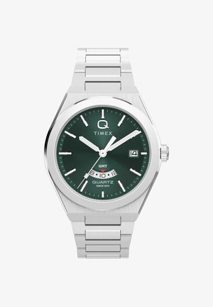 Ceas Timex cu carcasă metalică argintie, cadran verde, marcaje orare albe, fereastră pentru dată și subcadran GMT la ora 6.