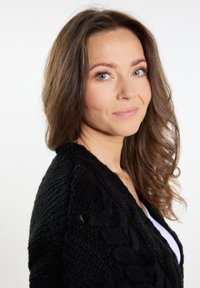 Černý pletený kardigan s copánkovým vzorem, s výstřihem do V a texturovaným povrchem. Modelka má vlnité vlasy a světlou pleť.