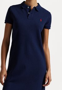 Námořnické polo šaty s límečkem, krátkými rukávy a malou červenou nášivkou na hrudi, vyrobené z texturované bavlny.