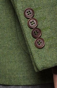 Zielona kurtka tweedowa o teksturowanym materiale, z czterema ciemnoczarnymi guzikami na mankiecie i subtelnymi detalami w szyciu.