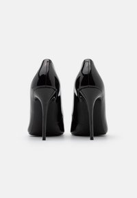 Talons hauts en cuir verni noir avec un bout pointu et un talon aiguille, présentant une surface lisse et un design minimaliste.