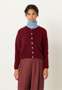 Burgundska pletena jakna z okroglim izrezom, dolgimi rokavi in petimi roza gumbi spredaj. Ujemajoče se s prostornimi maroon hlačami.