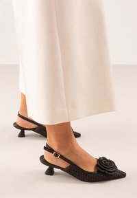 Zapatos negros de tipo slingback con punta afilada, diseño tejido texturizado, acento en forma de rosa y un pequeño tacón acampanado. Fabricados en material sintético.