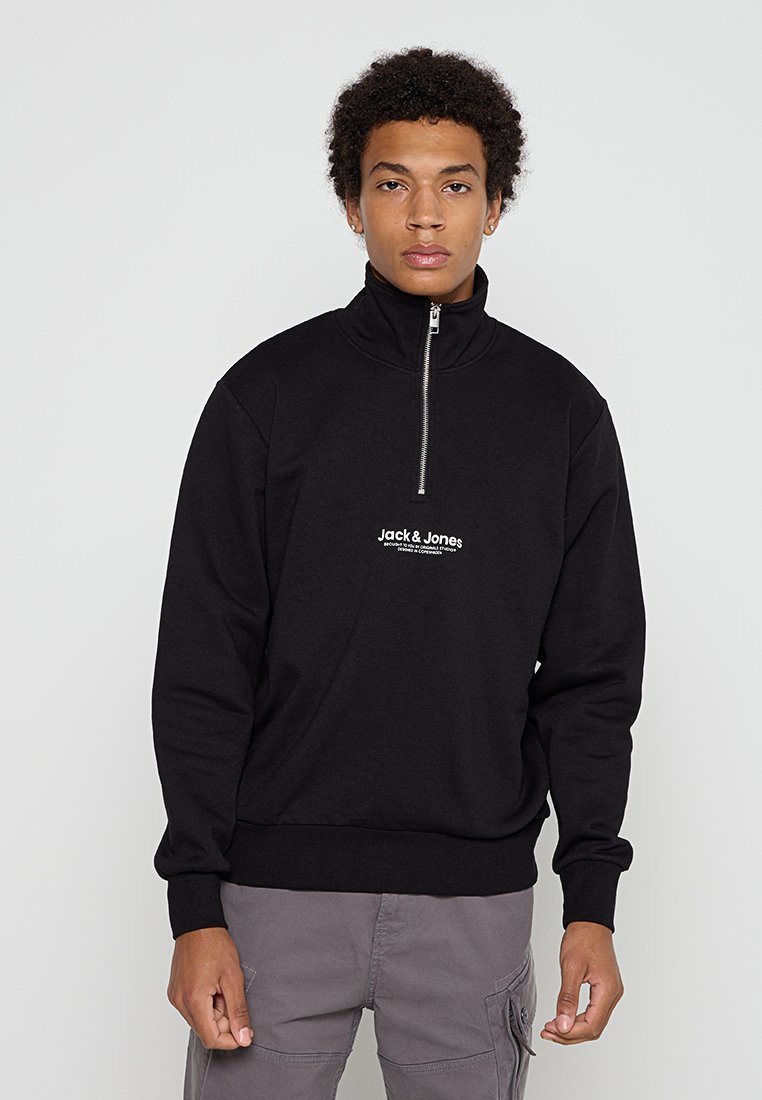 Sudadera con cremallera negra hecha de una tela suave. Presenta un cuello alto, puños acanalados y un logo blanco de "Jack & Jones" en la parte delantera.
