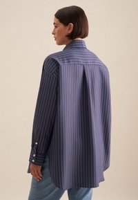 Camicia a righe blu navy con vestibilità rilassata, dotata di piega sul retro, polsini con bottoni e una texture di tessuto liscia.