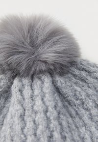 Grijze gebreide muts met kabelpatroon en zachte grijze bontlook pompon bovenop. De textuur lijkt dik en gezellig.