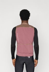 Lahka brezrokavnik v burgundski barvi z rjavimi dodatki. Ima zadržno žep in logo na hrbtni strani. Teksturirana tkanina zagotavlja zračnost.