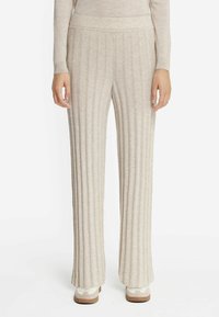 Jasno beżowe, ryflowane spodnie z szerokimi nogawkami i elastycznym pasem. Miękka tekstura, długość do podłogi, połączone z białymi sneakersami.