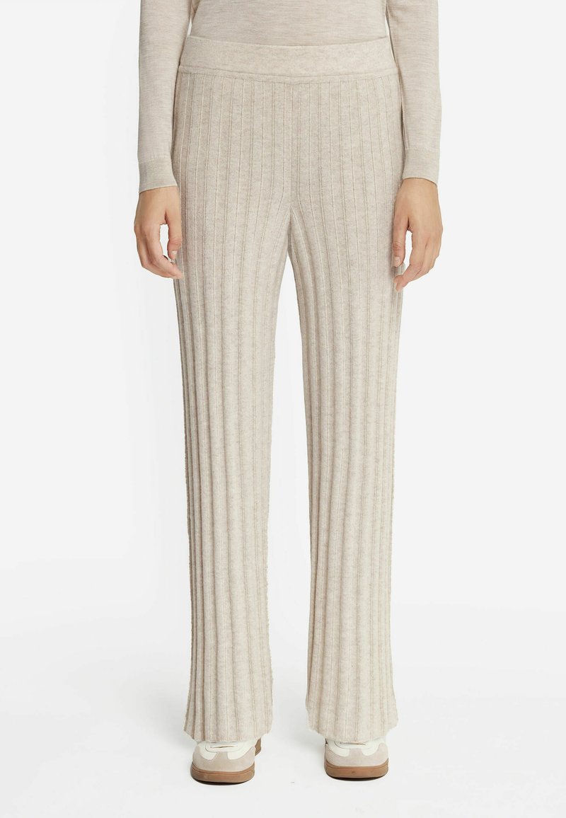 Jasno beżowe, ryflowane spodnie z szerokimi nogawkami i elastycznym pasem. Miękka tekstura, długość do podłogi, połączone z białymi sneakersami.