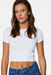 White cropped t-shirt made of soft cotton, featuring short sleeves and a round neckline, paired with blue denim high-waisted jeans.