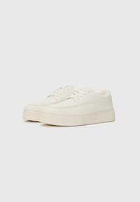 Weiße Schnürsneaker mit einer glatten Lederoberfläche, strukturiertem Plattformsohle und dezentem Branding auf der Zunge. Abgerundete Zehenform.