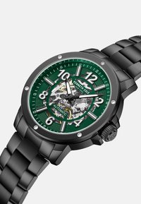 Zwarte roestvrijstalen automatische horloge met een groene gestructureerde wijzerplaat, zilveren uurmarkeringen en een transparante kast, met een opvallende kroon.